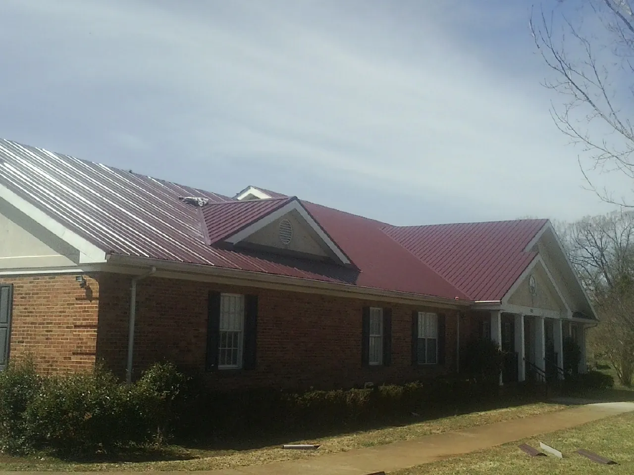 Red metal roof with gabled entries on a long brick building, from a Hail Damage Roof Repair job in Avinger