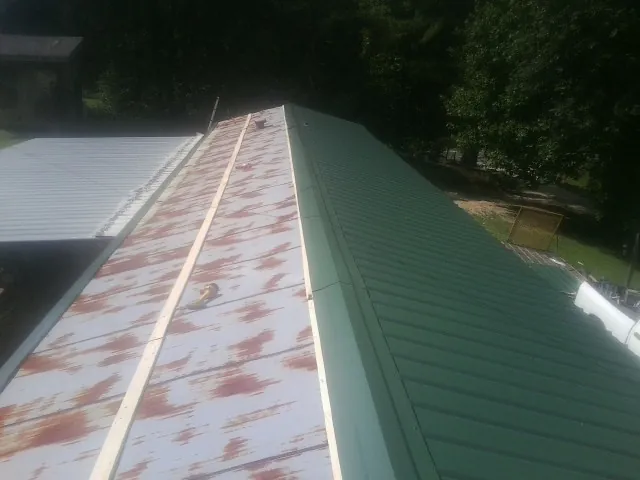 Old rusted panels beside newly installed green metal roofing — Wind Damage Roof Repair by Roofing Brothers in Avinger