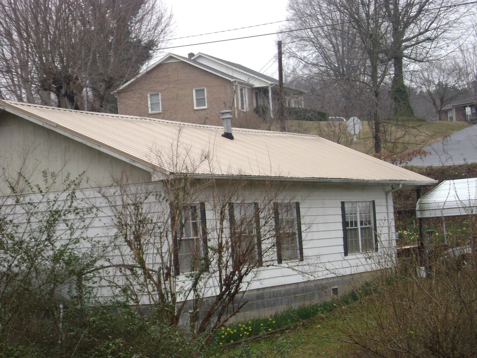 Tan metal roof on a white sided house set into a hillside — Commercial Roofing by Roofing Brothers in Avinger